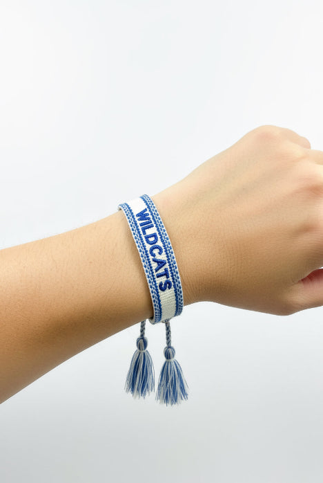 Blue and white woven bracelet with 'WILDCATS' text on a wooden surface