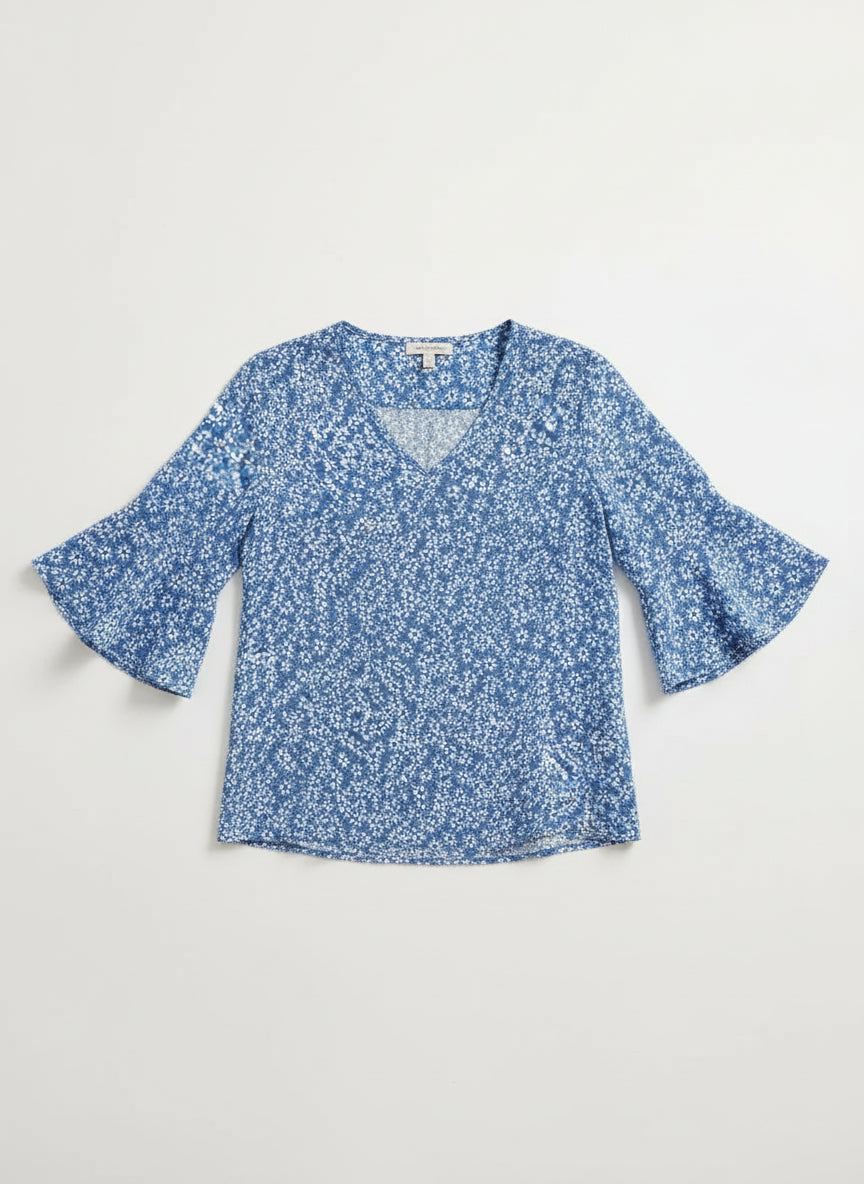 Woman wearing a blue floral blouse and white shorts on a light gray background