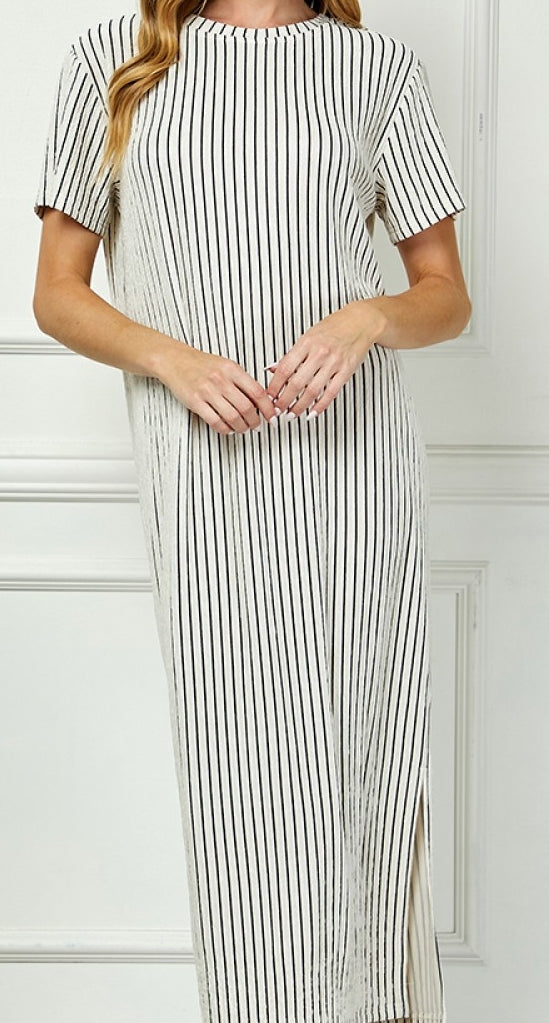 Woman wearing a black and white striped dress against a white wall.