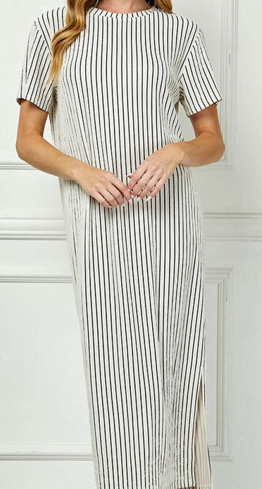 Woman wearing a black and white striped dress against a white wall.
