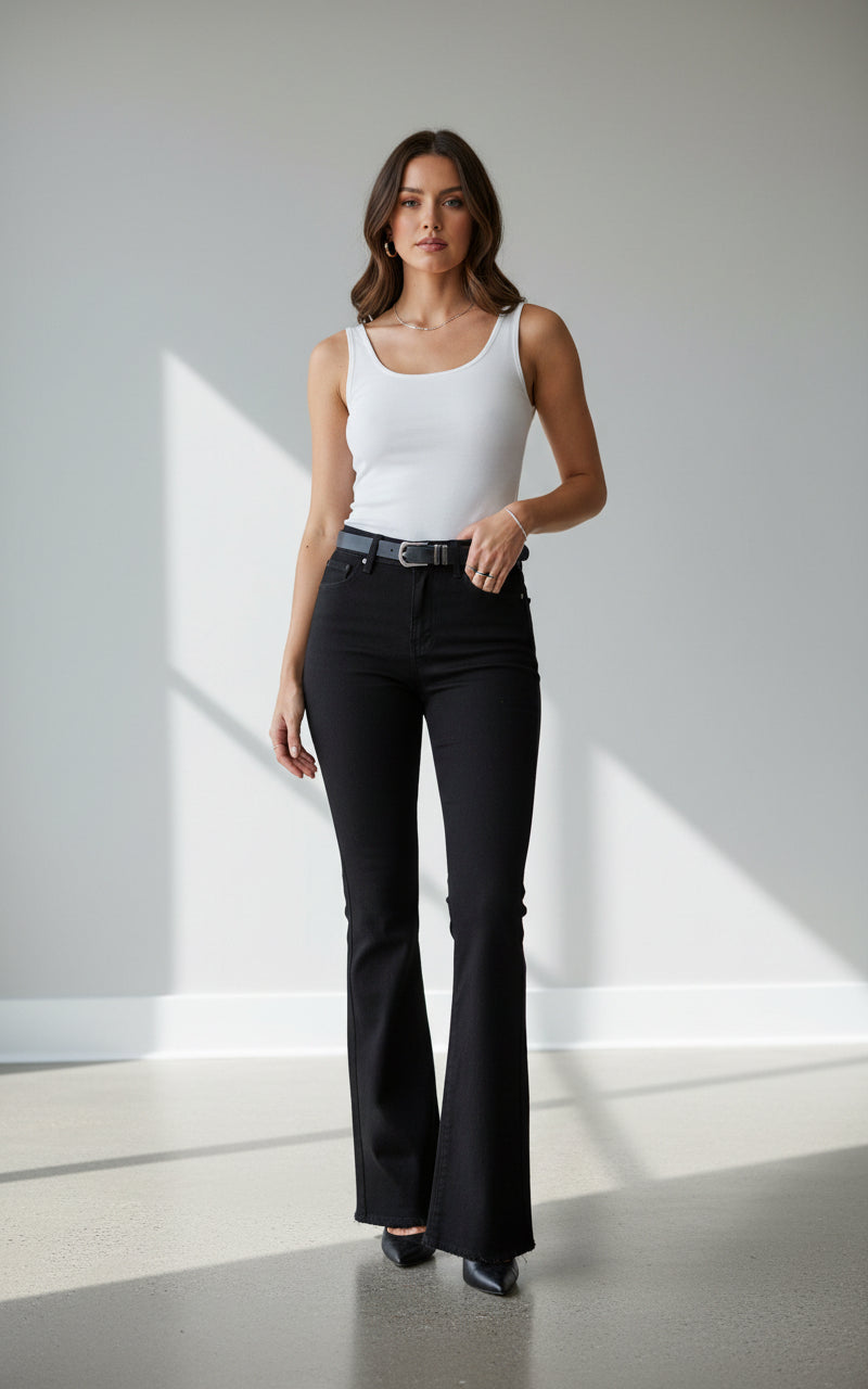 Woman wearing a white tank top and black flared pants on a gray background