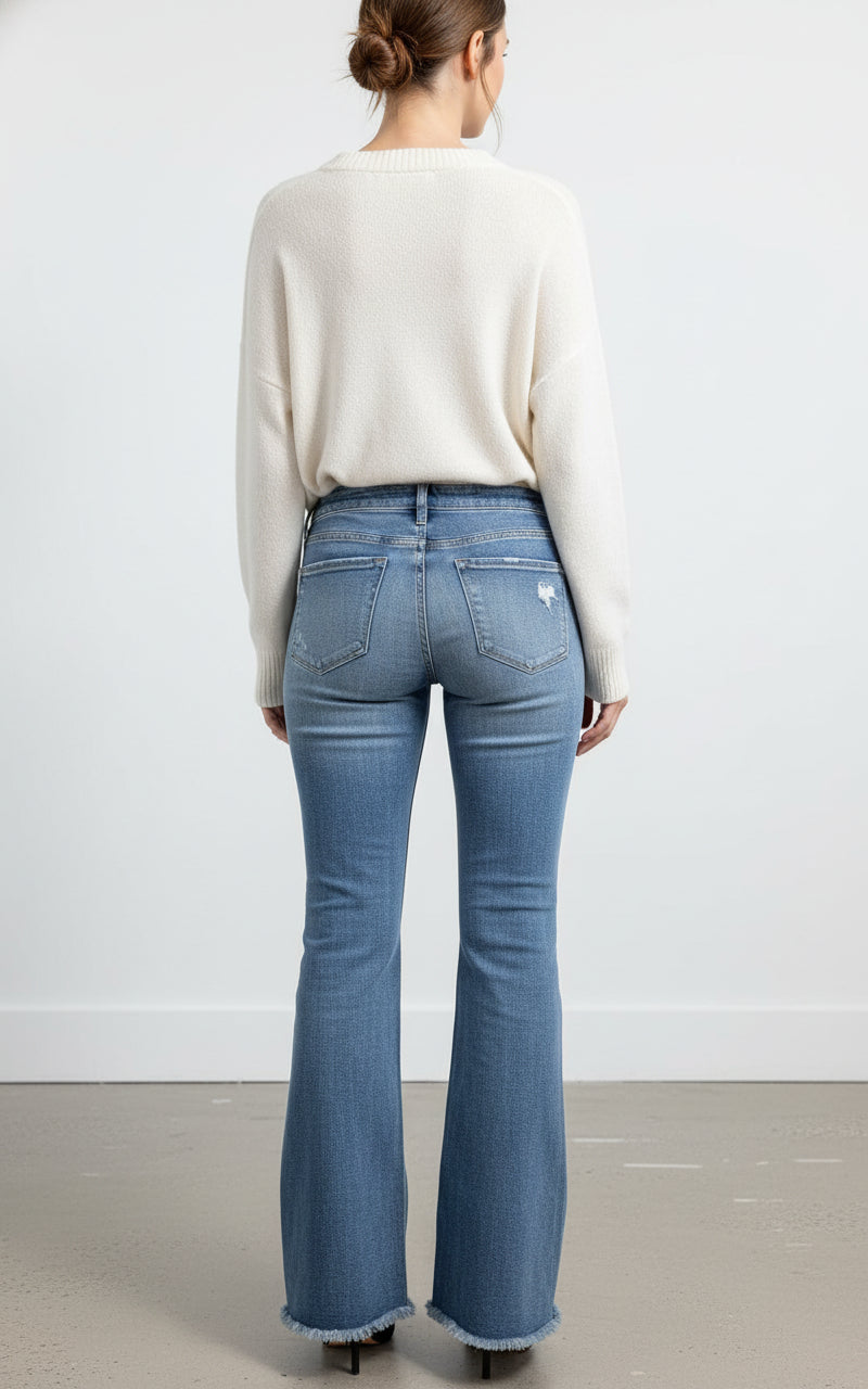 Person wearing blue flared jeans and a white sweater against a plain background