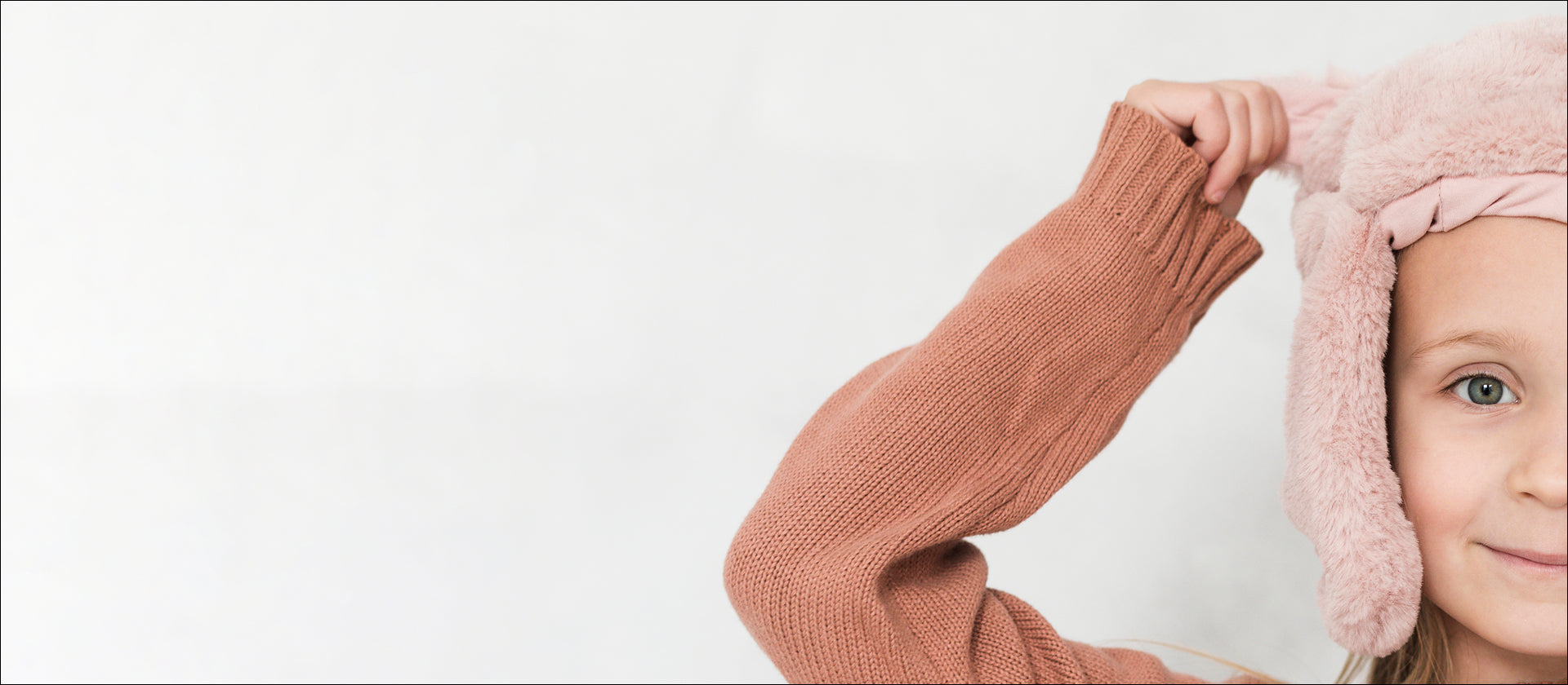 Child wearing a pink fleece-lined hat and brown sweater on a white background