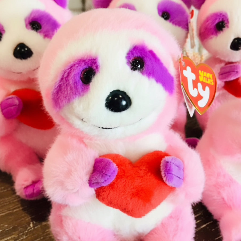 Plush toy sloth with pink fur, purple accents, and a red heart, featuring a Ty brand tag.