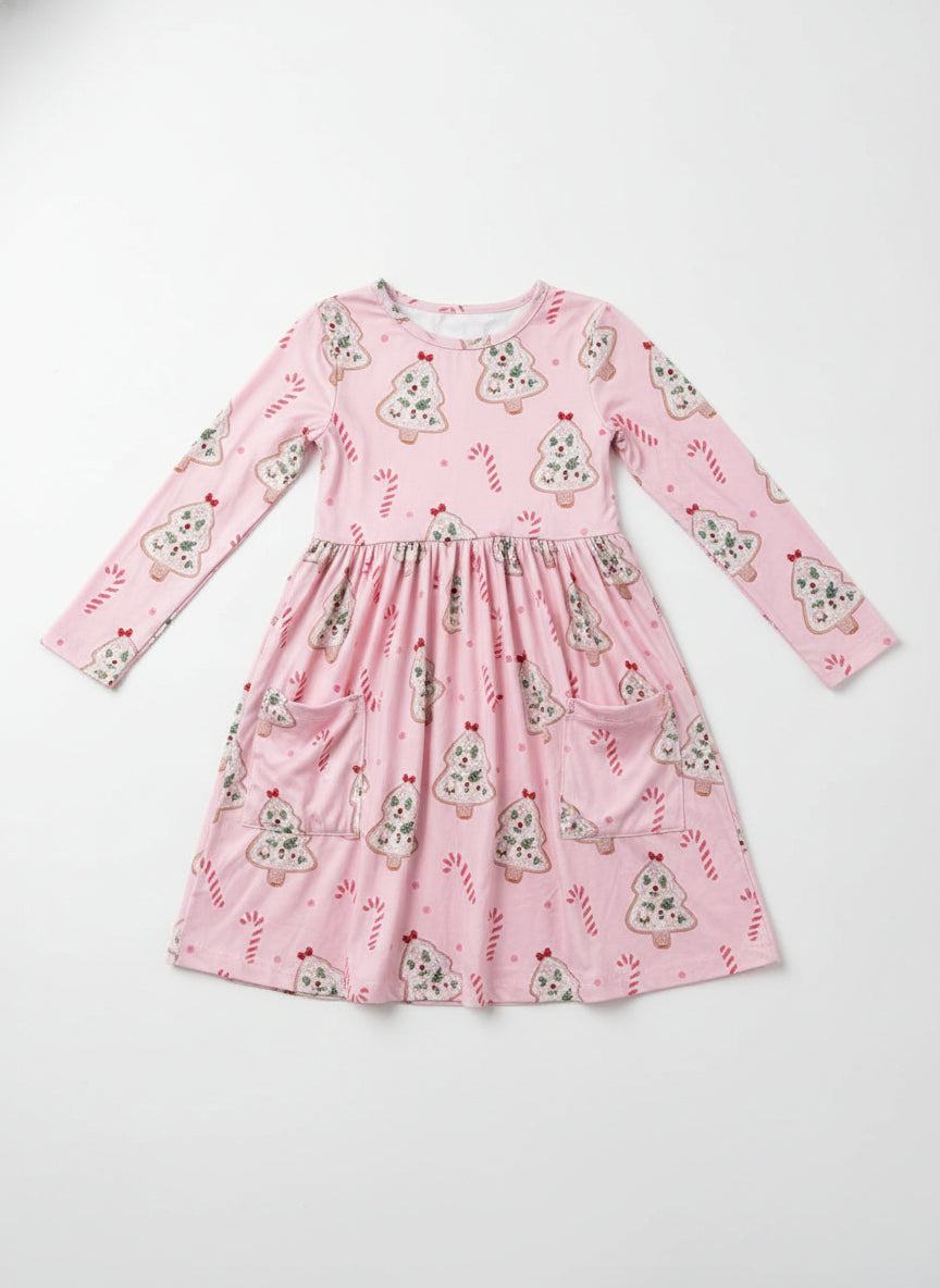 Young girl wearing a pink dress with a floral pattern in front of a brick wall.