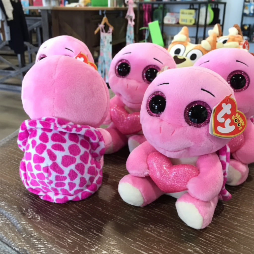 Pink plush toys with a visible brand tag on a wooden surface