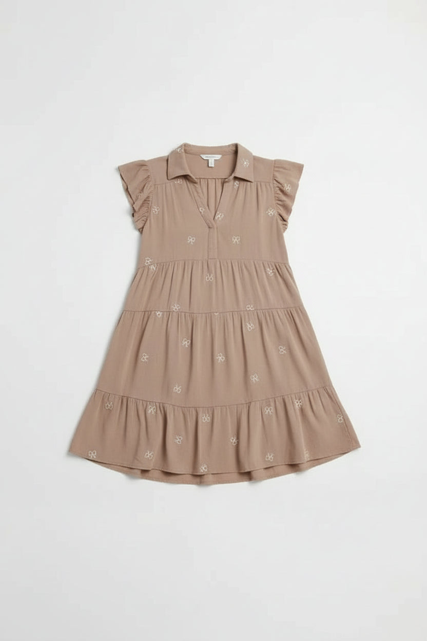 Woman wearing a brown dress with floral embroidery on a light gray background